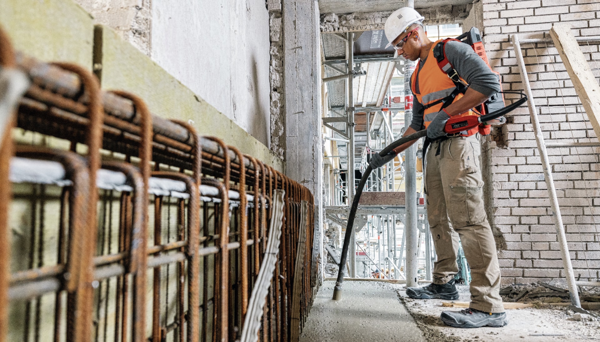 Worker using the NCV Cordless concrete vibrator indoors, vibrating a strip of concrete, free of gas fumes.